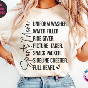 May include: White t-shirt with black text that reads "Sports Mom" and a list of duties: "Uniform Washer, Water Filler, Ride Giver, Picture Taker, Snack Packer, Sideline Cheerer, Full Heart."