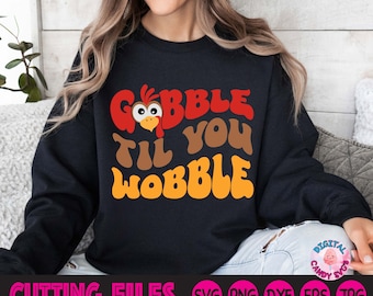 Może przedstawiać: Czarny sweter z napisem "Gobble Til You Wobble" w retro stylu. Głowa kreskówkowego indyka znajduje się w "G" od Gobble.