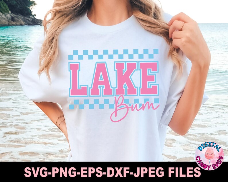 May include: White t-shirt with the text "LAKE Bum" in pink and blue. The word "LAKE" is in a block letter style with a checkered pattern above and below. The word "Bum" is in a cursive font.