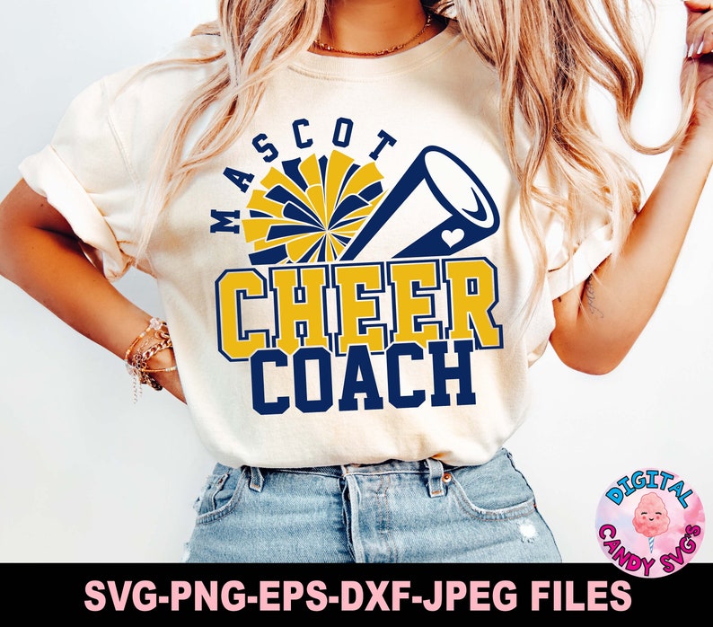 May include: A white t-shirt with a blue and yellow graphic design that says "Mascot Cheer Coach". The graphic includes a cheerleader's pom pom and a megaphone.