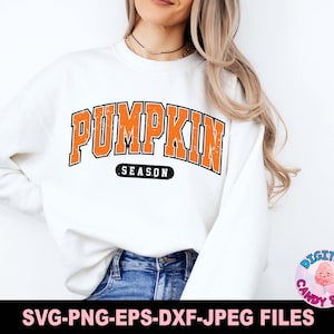 May include: A white sweatshirt with the text "PUMPKIN SEASON" in orange letters with a distressed look. The text is in a large, bold font and is centered on the sweatshirt.