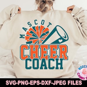 May include: A white sweatshirt with the text "MASCO7 CHEER COACH" in teal and orange. The design includes a teal and orange cheerleader pom-pom and a teal megaphone with a heart.
