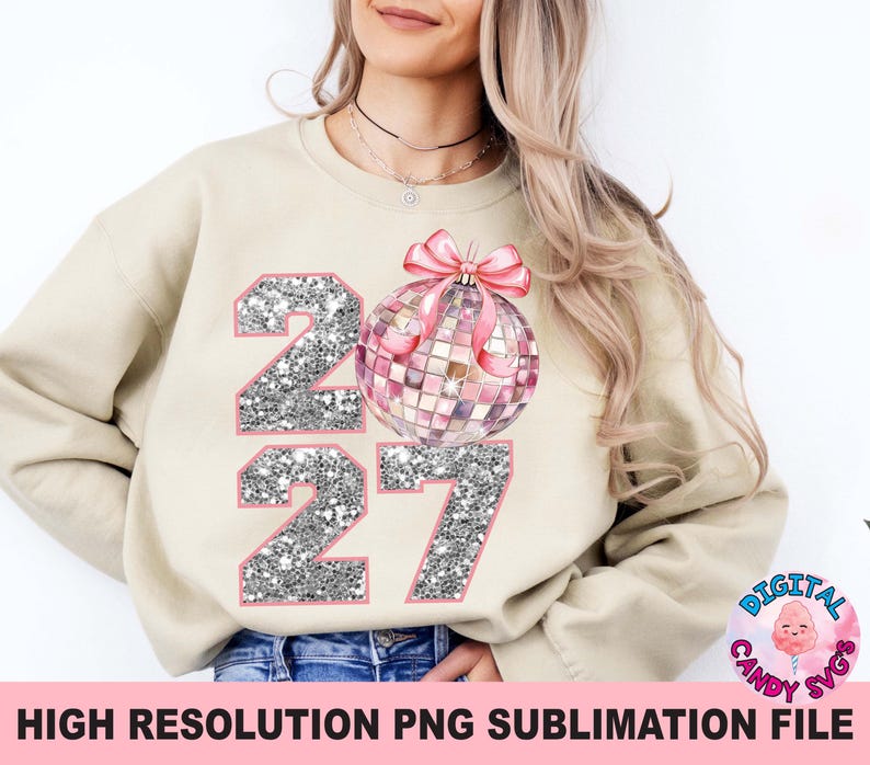 May include: A beige crewneck sweatshirt featuring a graphic of the year 2027 in silver glitter with pink outlines. A pink disco ball ornament with a pink bow is positioned between the numbers, replacing the zero in the year 2027 design.