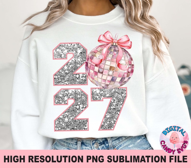 May include: A white long-sleeve sweatshirt featuring a graphic print of the number 2027 in silver glitter with pink outlines. A pink disco ball ornament with a pink ribbon bow is positioned above the number seven, replacing the zero.