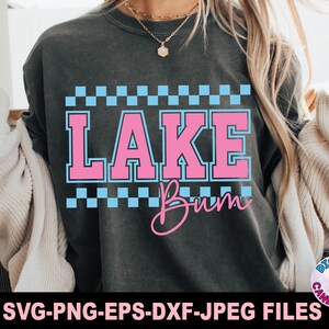 May include: Dark gray sweatshirt with the words "LAKE Bum" in pink and blue. The text is framed by a blue and white checkered pattern. The bottom of the image has the text "SVG-PNG-EPS-DXF-JPEG FILES".