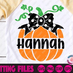 May include: A white and tan raglan shirt featuring an orange pumpkin design with a black polka dot bow and the name "Hannah" in black. The design includes green vines and the words "CUTTING FILES" at the bottom.