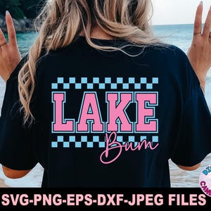 May include: Black t-shirt with the words "LAKE Bum" in pink and white, with a checkered pattern above. The shirt also has the text "SVG-PNG-EPS-DXF-JPEG FILES" at the bottom. The shirt is a casual style.