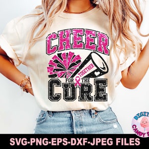 Puede incluir: Una camiseta blanca con un diseño de purpurina rosa que dice "Cheer for the Cure" con una cinta rosa y un pompón de purpurina negro y blanco.