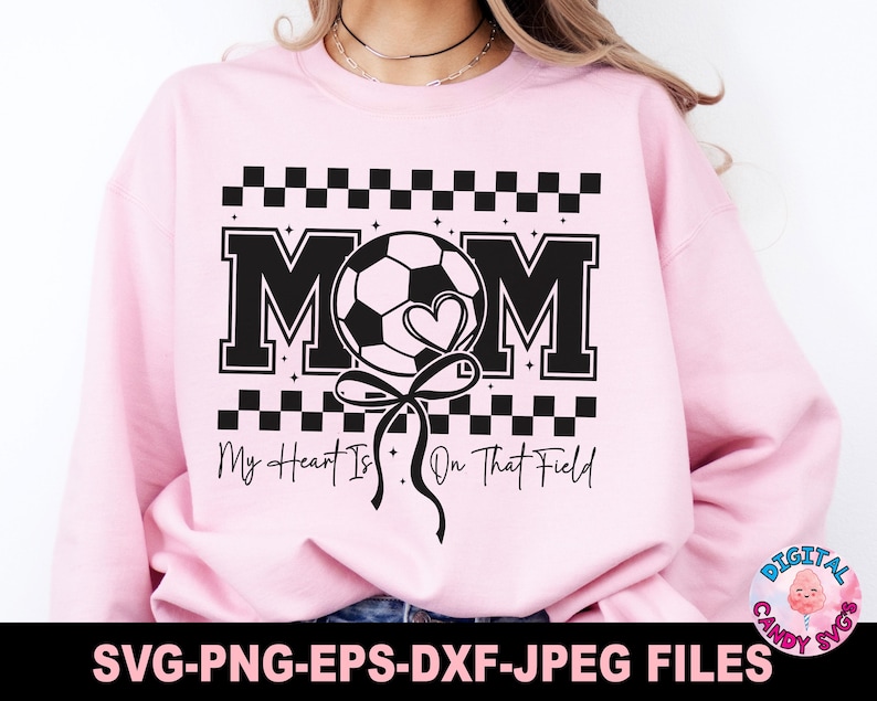 May include: Pink sweatshirt with a black and white checkered design. The text "MOM" is in large black letters with a black and white soccer ball and a heart in the middle. The text "My Heart Is On That Field" is below the design.