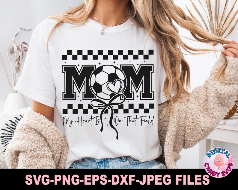 May include: White t-shirt with a black and white checkered design. The text "MOM" is in black with a white soccer ball and heart graphic. The text "My Heart Is On That Field" is below the graphic.