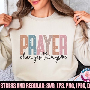 Peut inclure: Un sweat-shirt blanc avec le texte "PRAYER changes things" dans une police colorée et usée. Le texte est en nuances de rose, bleu et marron. Le texte est centré sur le sweat-shirt.