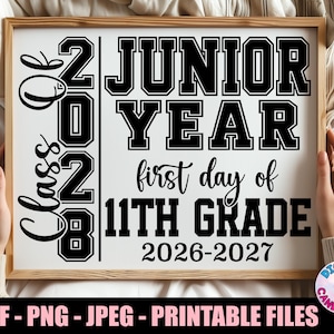 May include: A rectangular sign with black text on a white background. The text reads Class of 2028, Junior Year, first day of 11th Grade, and 2026-2027. The design features a mix of bold block lettering and a cursive script font style.
