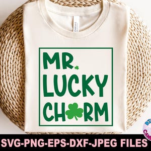 Puede incluir: Una camiseta blanca con un gráfico verde que dice "MR. LUCKY CHORM" con un diseño de trébol.