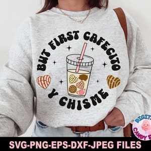 May include: A gray sweatshirt with the text "But first cafecito y chisme" in black and white. The text is surrounded by a circle with a brown and pink heart on each side. Inside the circle is a glass of iced coffee with brown and pink pastries.