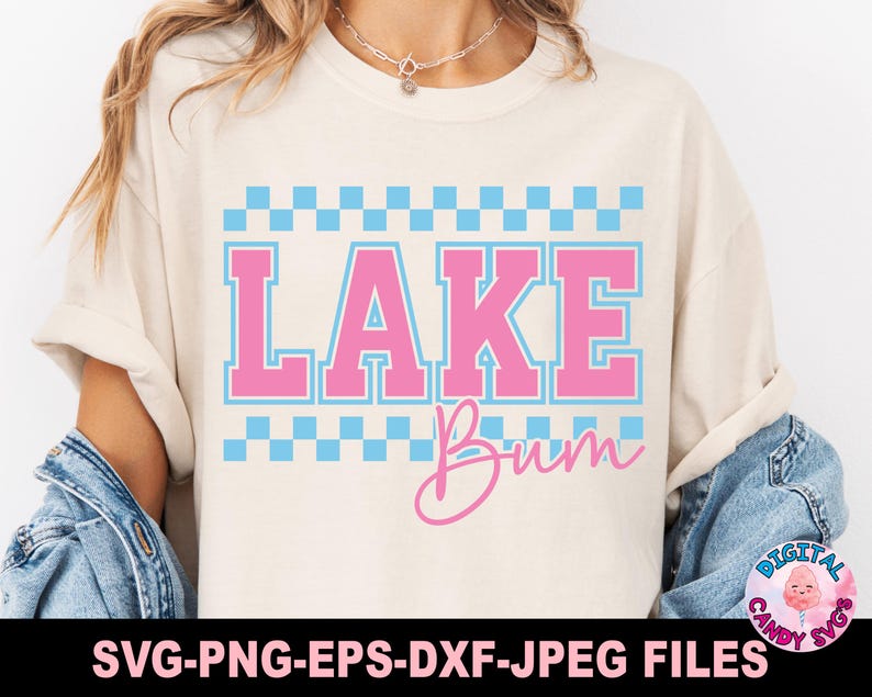 May include: Cream-colored t-shirt with the words "LAKE Bum" in pink and blue. The word "LAKE" is in a bold, collegiate-style font, with a blue checkered pattern above and below. The word "Bum" is in a cursive script.