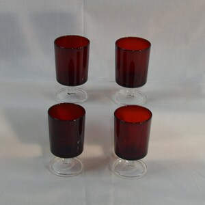 May include: Set of four red glass stemmed drinking glasses. The glasses are clear with a red tint and have a short stem.