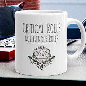 May include: White ceramic mug with a black and white illustration of a twenty-sided die with the text "Critical Rolls Not Gender Roles".