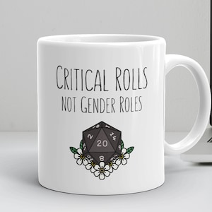 May include: White ceramic mug with a black graphic of a twenty-sided die with the text "Critical Rolls Not Gender Roles".