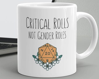May include: White ceramic mug with a black and white graphic that says "Critical Rolls Not Gender Roles". The graphic also includes a stylized orange 20-sided die with white numbers and green outlines. The die is surrounded by white flowers.
