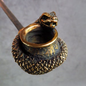May include: A brass smoking pipe with a snake head design. The pipe bowl is decorated with a scaly pattern and the stem is made of metal.