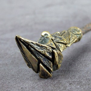 May include: A close-up of a bronze wand with a textured, geometric handle and a pointed tip. The wand's design suggests a fantasy theme. The wand's overall aesthetic is reminiscent of a magical item.