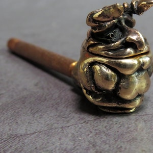 May include: A brass pipe with a detailed, textured, and whimsical design in the shape of a creature's head. The pipe has a long, thin stem.