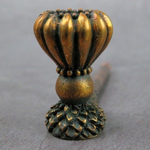 Puede incluir: Un pomo de puerta de metal dorado con una parte superior decorativa en forma de flor acanalada y una base texturizada y puntiaguda.