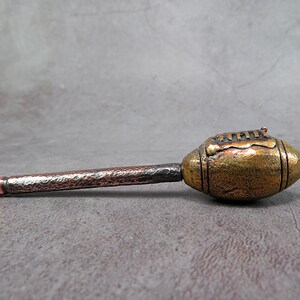 Puede incluir: Una pipa de metal con forma de balón de fútbol con un acabado de cobre texturizado. La pipa mide aproximadamente 18 cm de largo.