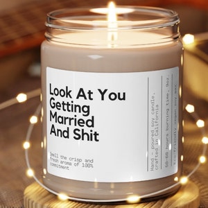 May include: A brown soy candle in a clear glass jar with a white label that reads "Look At You Getting Married And Shit". The candle is hand-poured and crafted in California. It has a 50-60 hour burn time and is made with eco-friendly vegan soy wax.