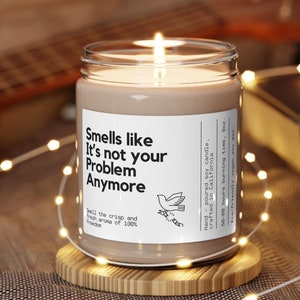 May include: A brown soy candle with a white label that reads "Smells like It's not your Problem Anymore". The candle is sitting on a wooden coaster and surrounded by white fairy lights.