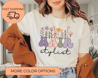 May include: White t-shirt with a floral design and the text "HAIR stylist" in colorful, retro-style letters.