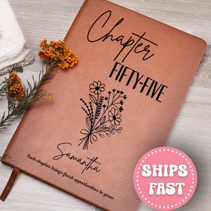 May include: A brown leather journal with the words "Chapter FIFTY-FIVE" and the name "Samantha" printed on the cover. A floral bouquet design is also featured. The journal includes the quote, "Each chapter brings fresh opportunities to grow."