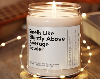 May include: A clear glass candle jar with a beige soy candle inside. The candle is labeled "Smells Like Slightly Above Average Bowler". The label also says "Hand-poured soy candle, crafted in California. 50-60 hours burning time, 9oz. Eco-friendly vegan soy wax."