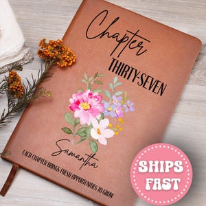 May include: A brown leather journal with the words "Chapter THIRTY-SEVEN" in black script. The journal is decorated with a floral design in pink, purple, and white. The name "Samantha" is written below the flowers. The text "Each chapter brings fresh opportunities to grow" is at the bottom.