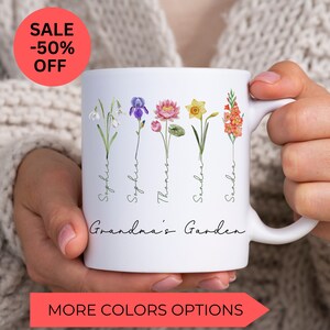 May include: White ceramic mug with a floral design and the text "Grandma's Garden". The flowers are watercolor illustrations of snowdrops, irises, lotuses, daffodils, and gladiolus. The names "Sophia", "Sophia", "Thomas", "Sandra", and "Sandra" are written vertically along the stems of the flowers.