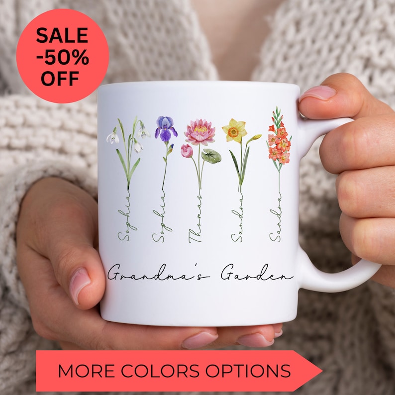 May include: White ceramic mug with a floral design and the text "Grandma's Garden". The flowers are watercolor illustrations of snowdrops, irises, lotuses, daffodils, and gladiolus. The names "Sophia", "Sophia", "Thomas", "Sandra", and "Sandra" are written vertically along the stems of the flowers.