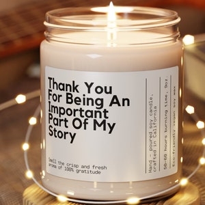 May include: A glass candle jar with a white label that reads "Thank You For Being An Important Part Of My Story". The candle is lit and the jar is surrounded by string lights.