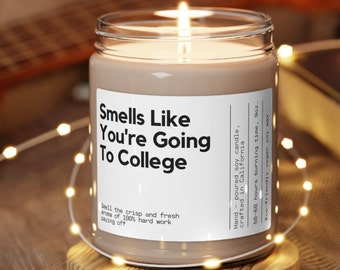 May include: A brown soy candle in a clear glass jar with a white label that reads "Smells Like You're Going To College". The label also includes the text "Hand-poured soy candle, crafted in California. 50-60 hours burning time, 9oz. Eco-friendly vegan soy wax."