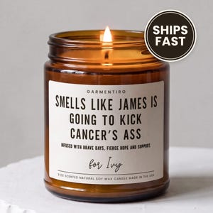 May include: A 9 oz amber glass jar candle with a white label featuring the text: GARMENTIRO, SMELLS LIKE JAMES IS GOING TO KICK CANCER'S ASS, INFUSED WITH BRAVE DAYS, FIERCE HOPE AND SUPPORT, for Ivy, 9 OZ SCENTED NATURAL SOY WAX CANDLE MADE IN THE USA.