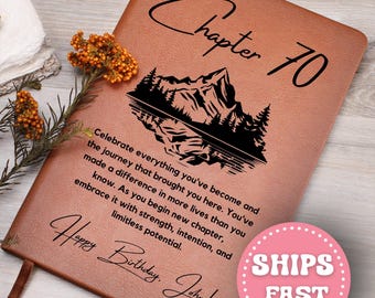 May include: Brown leather journal with the words "Chapter 70" and "Happy Birthday, John!" in black script. A mountain and forest silhouette is featured. The journal includes inspirational text.