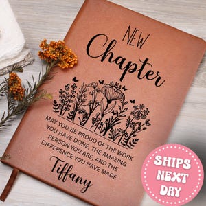 May include: A brown leather journal with the words "New Chapter" in elegant script. The journal features a floral design and the text "May you be proud of the work you have done..." and the name "Tiffany".