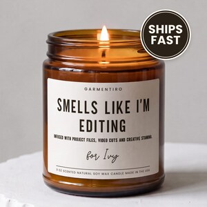 May include: A 9 oz scented natural soy wax candle in an amber glass jar with a lit wick. The white label features the text: GARMENTIRO, SMELLS LIKE I'M EDITING, INFUSED WITH PROJECT FILES, VIDEO CUTS AND CREATIVE STAMINA, for Ivy.