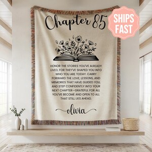 Puede incluir: Manta beige con texto «Capítulo 85», ilustración floral de libro y cita inspiradora. Cuenta con un borde con flecos y el nombre Olivia. Una pieza decorativa para la decoración del hogar.
