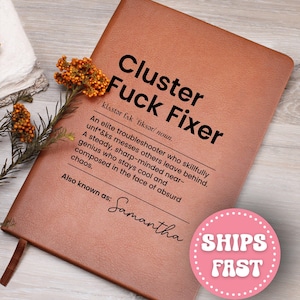 May include: A brown notebook with the text "Cluster Fuck Fixer" in bold black letters. The definition of the term is below the title. The name "Samantha" is written in cursive. A pink circle with the words "SHIPS FAST" is in the bottom right corner.