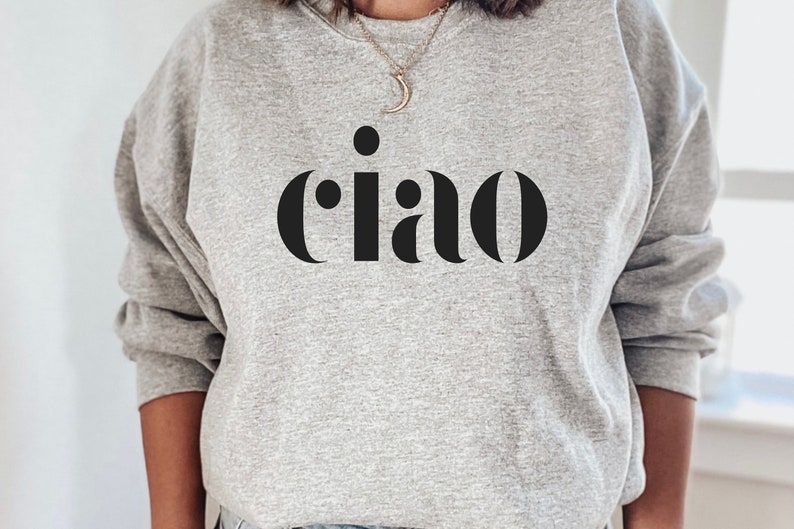 May include: A pale grey sweatshirt featuring the word "ciao" in large, black, sans-serif letters. The word is centered on the chest. The sweatshirt has long sleeves and a round neck.