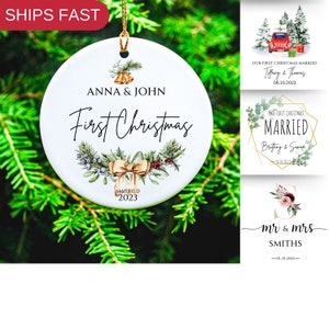 May include: White ceramic Christmas ornament with a green and gold floral wreath, the text "Anna & John First Christmas Married 2023" and gold bells.