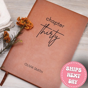 May include: A brown leather journal with the words "chapter thirty" in black script. The name "Olivia Smith" is printed at the bottom. A sprig of orange berries and greenery rests on the side.