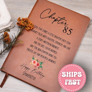 May include: A brown leather journal with the text "Chapter 85" and a floral design. The journal includes the text "Happy Birthday, Samantha" and other inspirational text. A pink circle with the words "SHIPS FAST" is in the lower right corner.
