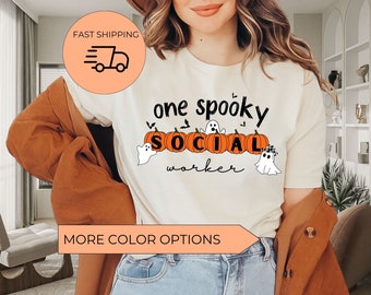 May include: White t-shirt with the text "one spooky social worker" in black lettering. The text is surrounded by orange pumpkins with white ghost faces and bats.
