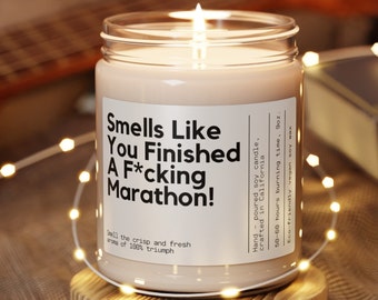 May include: A lit candle in a glass jar with a white label. The label reads "Smells Like You Finished A F*cking Marathon!". The candle is hand-poured soy wax and has a 50-60 hour burn time. The aroma is described as crisp and fresh.